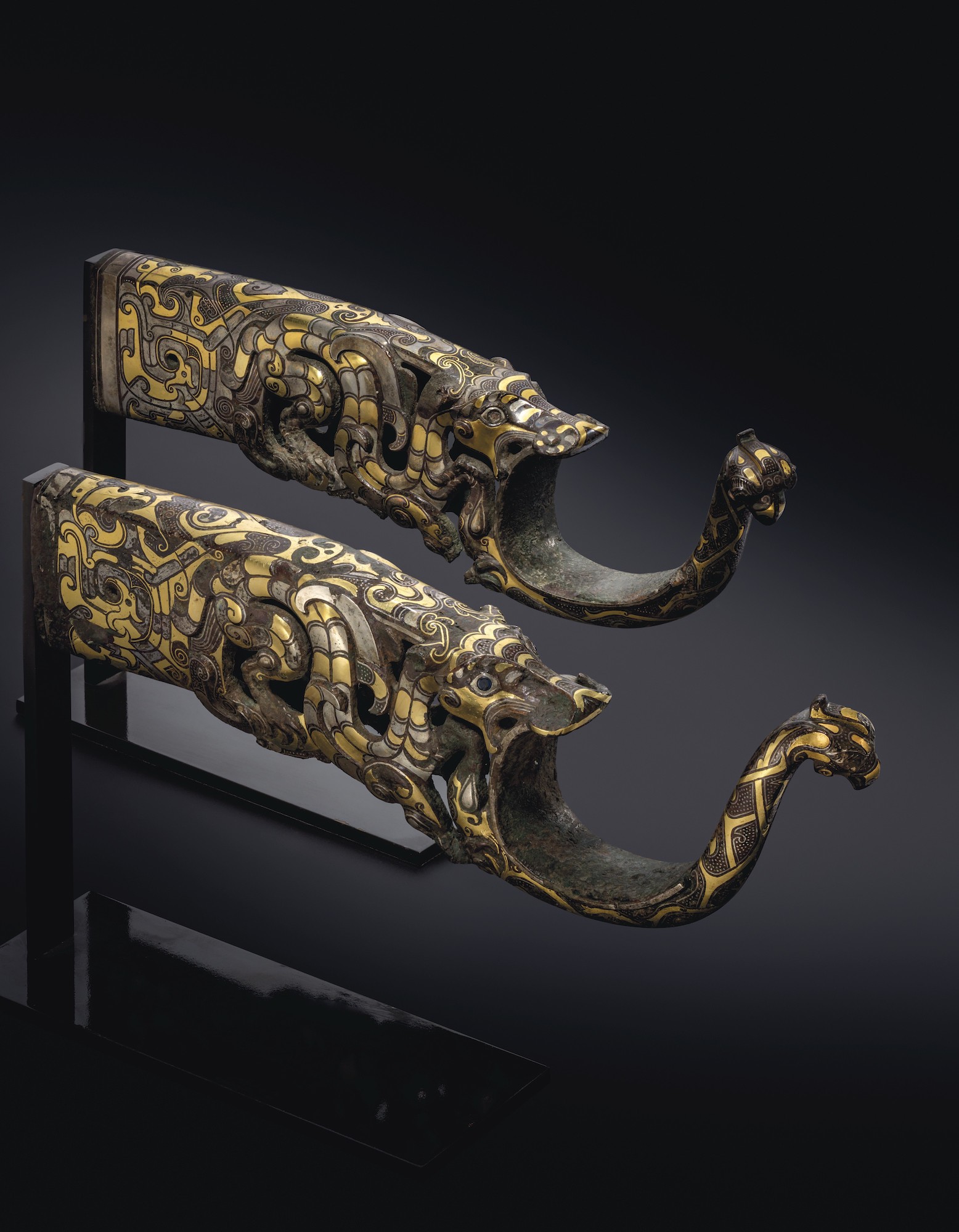 EASTERN ZHOU DYNASTY, 4TH-3RD CENTURY BC
The chariot fittings are exquisitely inlaid in gold and silver and skillfully cast in openwork in the zoomorphic form of a dragon pursuing a phoenix, the shaft in the form of a cross-bow support. The dragons are powerfully rendered with sinuous winged bodies inlaid in silver and gold with interlaced motifs, dots, striations and scale-shaped details. The three-claws of each front leg are hooked into the body of the phoenix that has an inclined head, blue-black glass eyes, sharp beak and curled crest. The interior of the bronze fittings have malachite patination and are heavily encrusted.
10 ¼ in. (26 cm.) long
Estimate 600,000 - 1,000,000 British pounds EASTERN ZHOU DYNASTY, 4TH-3RD CENTURY BC
The chariot fittings are exquisitely inlaid in gold and silver and skillfully cast in openwork in the zoomorphic form of a dragon pursuing a phoenix, the shaft in the form of a cross-bow support. The dragons are powerfully rendered with sinuous winged bodies inlaid in silver and gold with interlaced motifs, dots, striations and scale-shaped details. The three-claws of each front leg are hooked into the body of the phoenix that has an inclined head, blue-black glass eyes, sharp beak and curled crest. The interior of the bronze fittings have malachite patination and are heavily encrusted.
10 ¼ in. (26 cm.) long
Estimate 600,000 - 1,000,000 British pounds