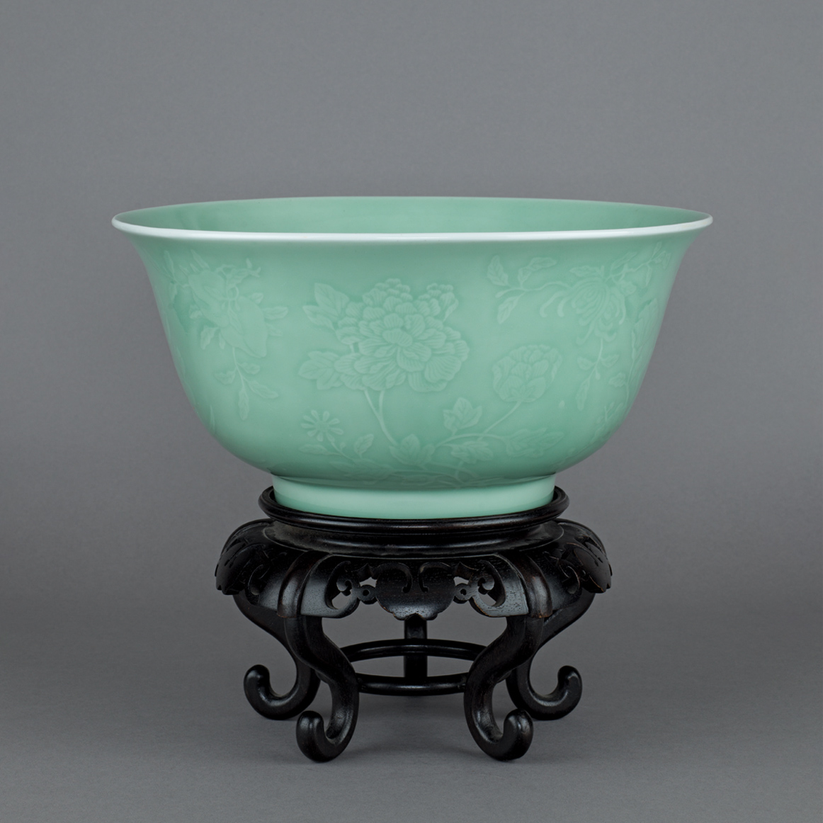 Chinese imperial porcelain large celadon-glazed moulded and carved deep bowl decorated on the exterior with large sprays of various flowers including; lotus, peach, peony, pink, finger citron, prunus, camellia, pomegranate, tree peony and lychee. The base with a six-character sealmark of Qianlong in underglaze blue and of the period, 1736-1795. 13 1/4 inches, 33.8 cm diameter. • From the collection of Dr. Ho-Ching (1900-1963) and Mme. Von Sung Yang (1903-2005), acquired between 1939 and 1955 and thence by descent, together with label E/O Von Sung Ya, 40026807 38DSL. Chinese imperial porcelain large celadon-glazed moulded and carved deep bowl decorated on the exterior with large sprays of various flowers including; lotus, peach, peony, pink, finger citron, prunus, camellia, pomegranate, tree peony and lychee. The base with a six-character sealmark of Qianlong in underglaze blue and of the period, 1736-1795. 13 1/4 inches, 33.8 cm diameter. • From the collection of Dr. Ho-Ching (1900-1963) and Mme. Von Sung Yang (1903-2005), acquired between 1939 and 1955 and thence by descent, together with label E/O Von Sung Ya, 40026807 38DSL.