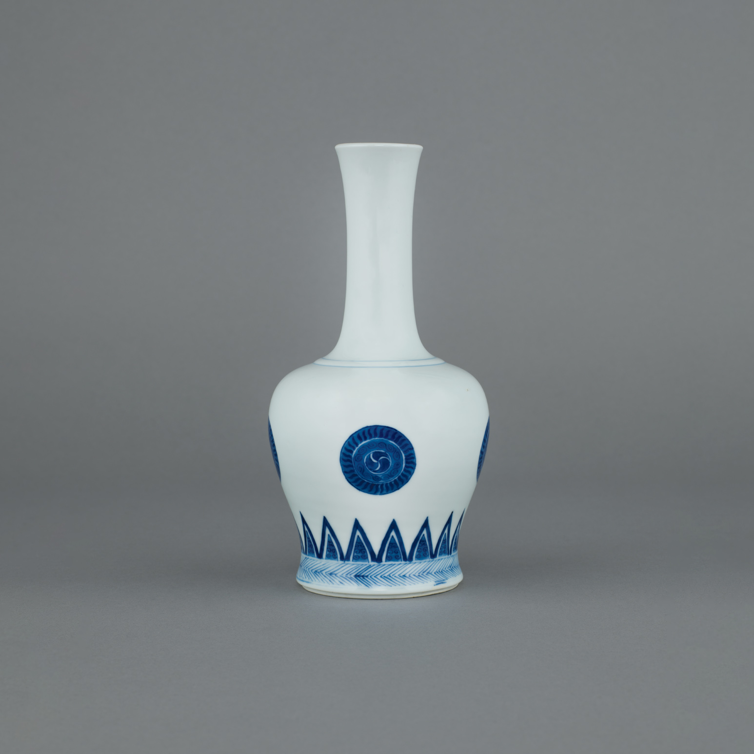 Chinese imperial porcelain blue and white slender necked baluster vase, of handbell form, yaoling zun, painted on the body with four circular medallions consisting of three bands forming the gankyil, “Wheel of Joy”. The base with a six-character mark of Kangxi within a double ring in underglaze blue and of the period, 1662-1722. 8 inches, 20.4 cm high. • Sold by Sotheby’s London in their auction of Fine Chinese Ceramics and Works of Art, 15th June 1982, lot 357, pp. 248/9. • Spink and Son, 1982. • From the collection of Mr H. Soudovar. Chinese imperial porcelain blue and white slender necked baluster vase, of handbell form, yaoling zun, painted on the body with four circular medallions consisting of three bands forming the gankyil, “Wheel of Joy”. The base with a six-character mark of Kangxi within a double ring in underglaze blue and of the period, 1662-1722. 8 inches, 20.4 cm high. • Sold by Sotheby’s London in their auction of Fine Chinese Ceramics and Works of Art, 15th June 1982, lot 357, pp. 248/9. • Spink and Son, 1982. • From the collection of Mr H. Soudovar.