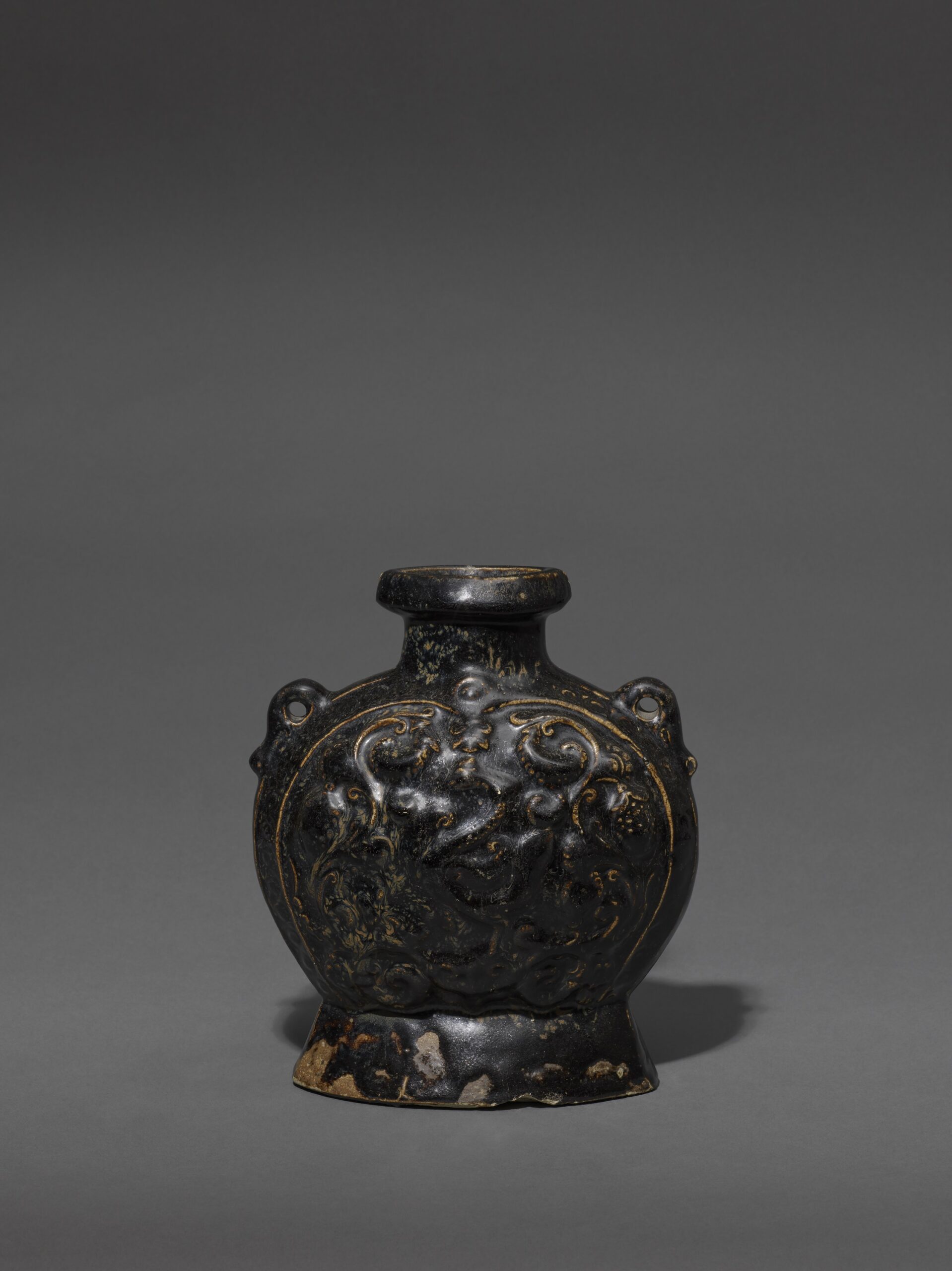 A BLACK-GLAZED STONEWARE PHOENIX-PATTERN PILGRIM FLASK Sui dynasty (581-618) or early Tang dynasty (618-906) Height: 23.2 cm, 9 ⅛ inches 隋或唐 黑釉瓷葡萄鳳紋扁壺 高23.2釐米 A BLACK-GLAZED STONEWARE PHOENIX-PATTERN PILGRIM FLASK Sui dynasty (581-618) or early Tang dynasty (618-906) Height: 23.2 cm, 9 ⅛ inches 隋或唐 黑釉瓷葡萄鳳紋扁壺 高23.2釐米